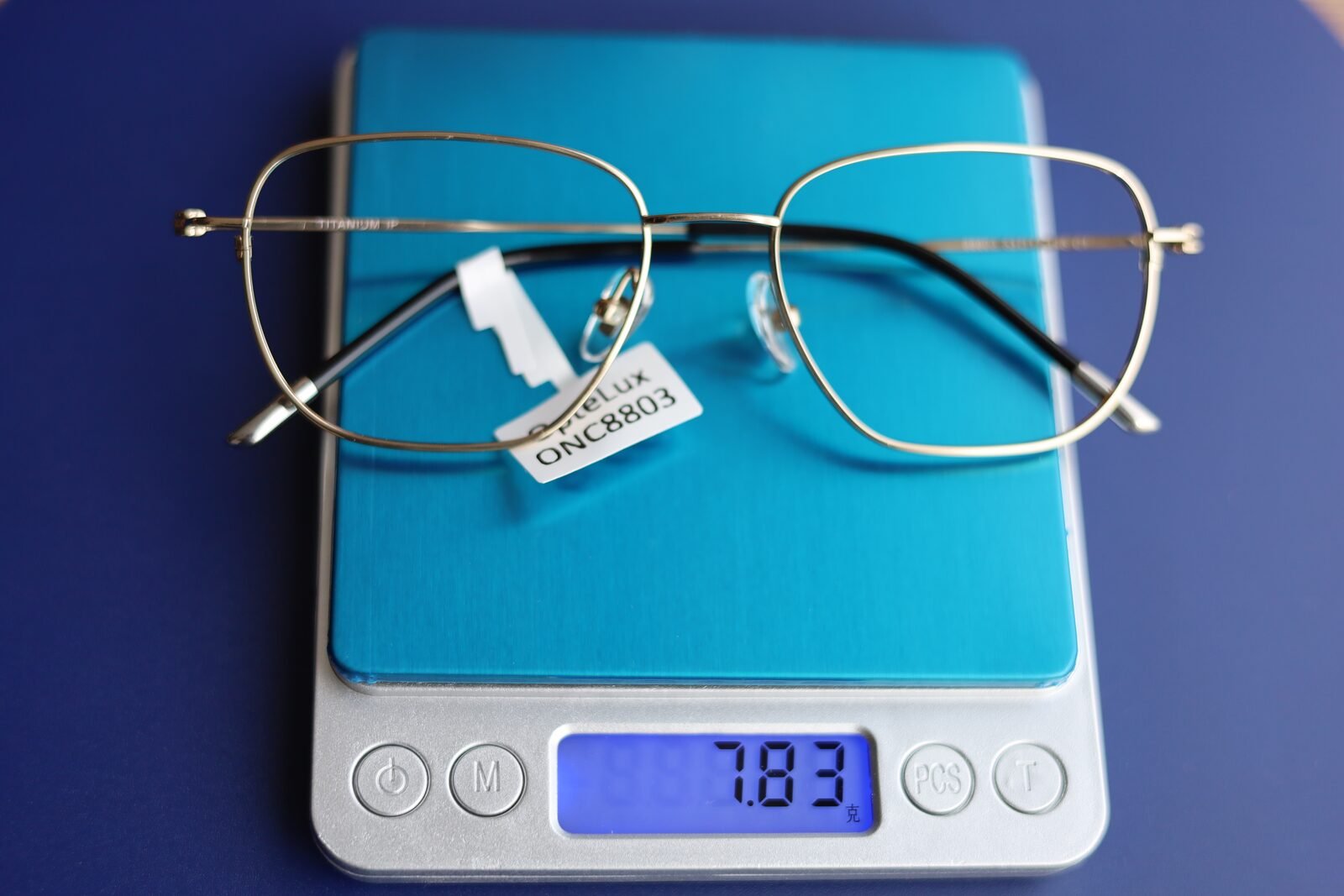 OpteLux ONC8803 titanium eyeglass frame on a jeweller’s scale reading 7.83 grams, frame only
