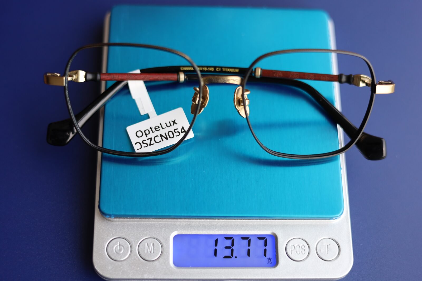 OpteLux OSZCN054 titanium eyeglass frame on a jeweller’s scale reading 13.77 grams, frame only